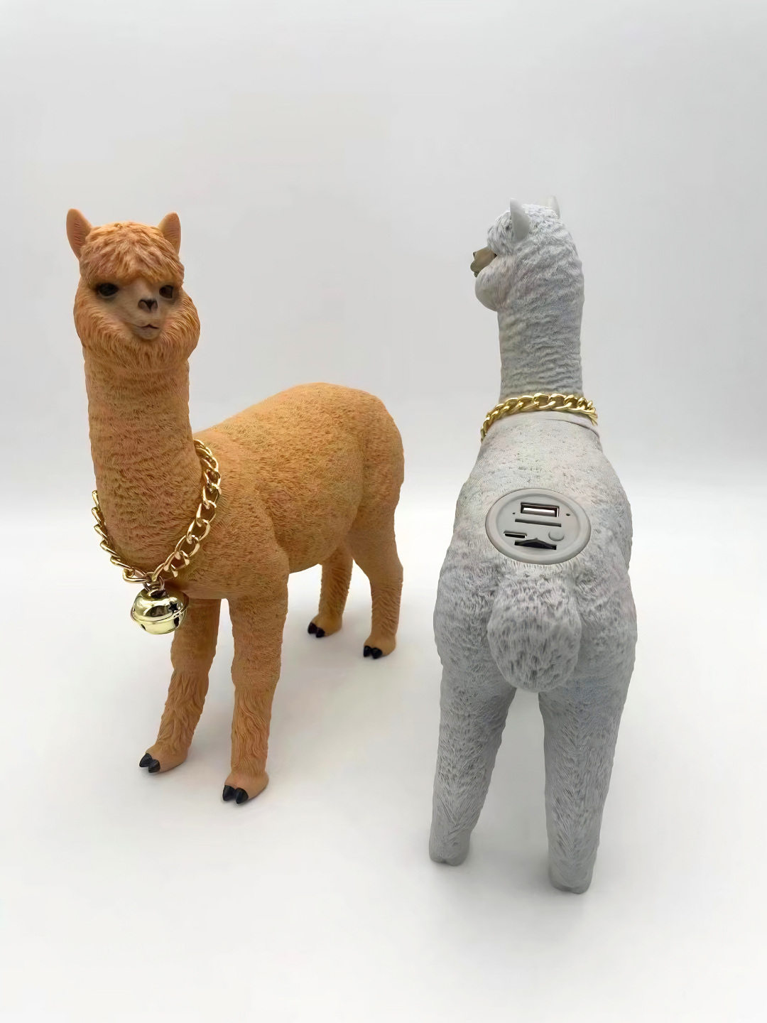 Due alpaca con collane dorate su sfondo bianco; la grigia mostra una porta USB sul dorso.