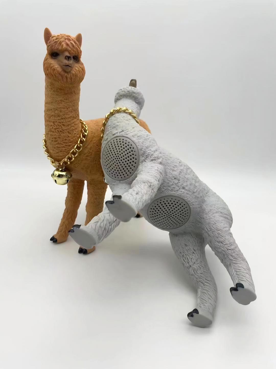 Due casse bluetooth alpaca, grigia con altoparlanti sul fianco e senape con collana dorata.