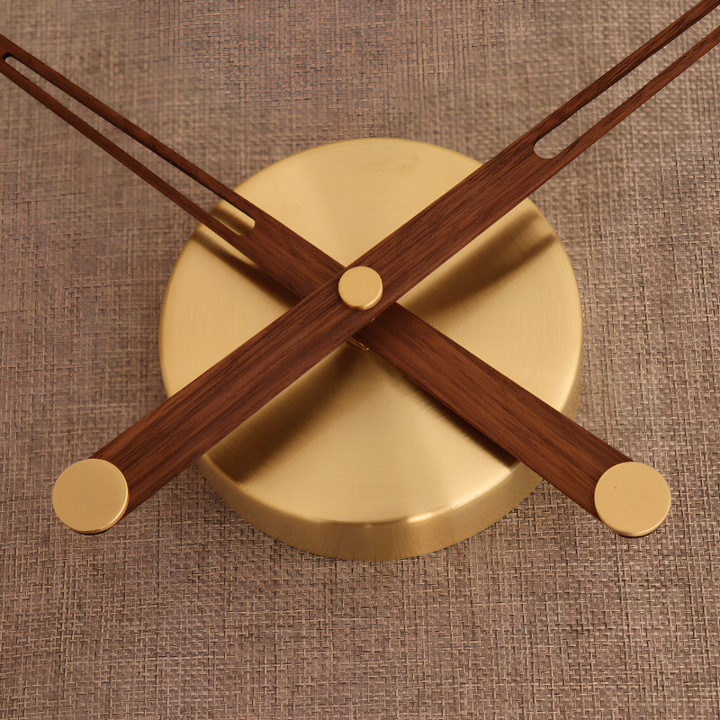Orologio da parete minimalista in noce con lancette incrociate su base dorata in metallo, diametro 60 cm.