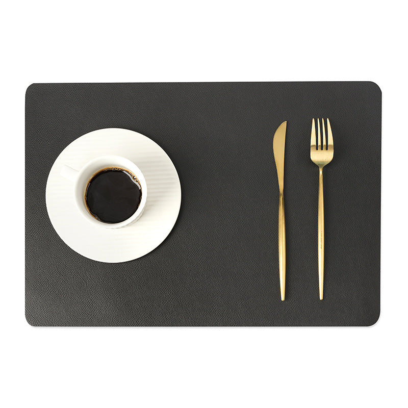Tovaglietta in ecopelle tinta unica grigio scuro, protezione dal calore, impermeabile; tazza bianca e posate dorate.