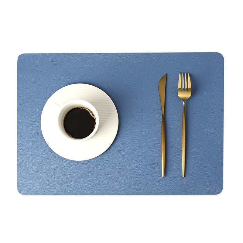 Tovaglietta in ecopelle tinta unita blu con tazza di caffè su piattino bianco e posate dorate.