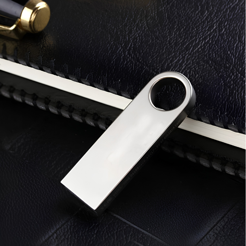 Chiavetta USB in metallo con foro circolare, poggiata su taccuino nero.