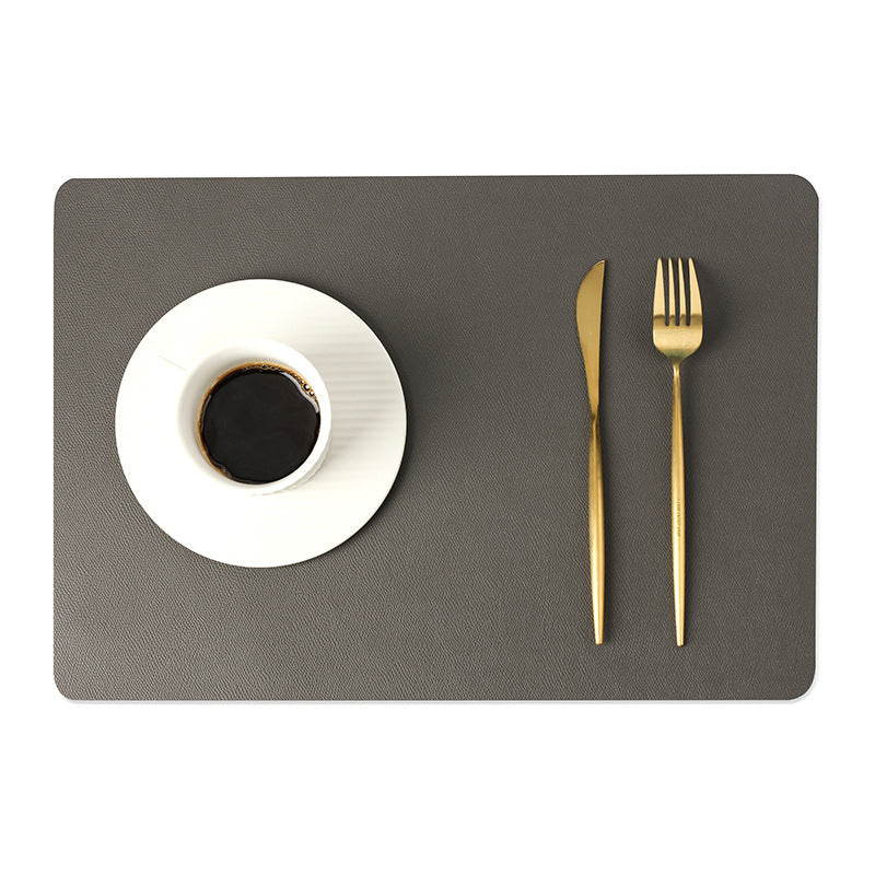 Sottopiatto in ecopelle grigio scuro con tazza di caffè e posate dorate.