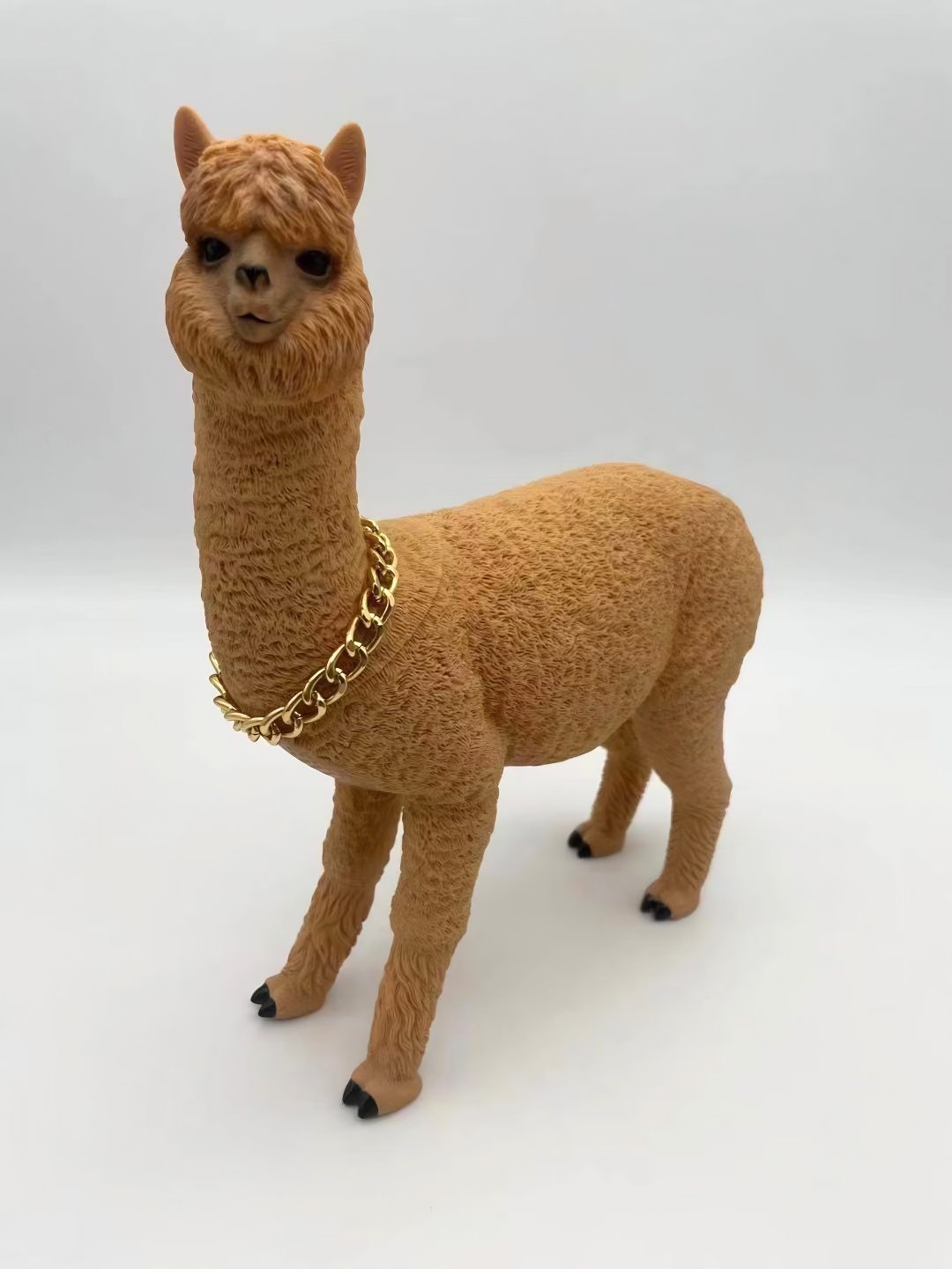 Alpaca di colore senape, con collana dorata, in piedi su sfondo bianco.