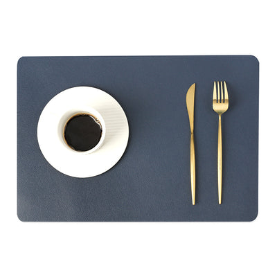 Tovaglietta in ecopelle blu navy con piatto bianco e posate dorate.