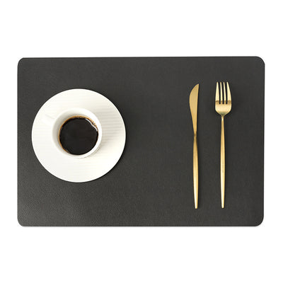 Tovaglietta in ecopelle tinta unica grigio scuro, protezione dal calore, impermeabile; tazza bianca e posate dorate.