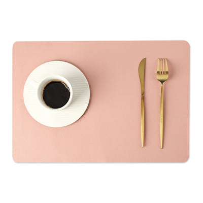 Sottopiatto in ecopelle a tinta unita rosa pesca, resistente al calore e agli oli, con tazza e posate dorate.