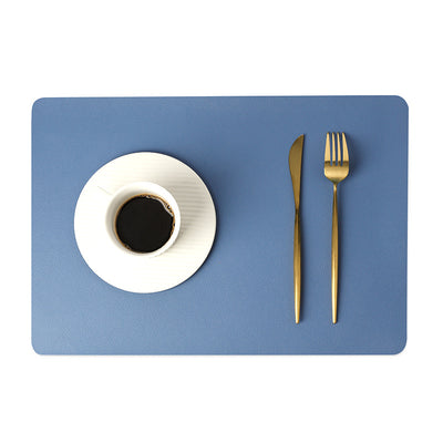 Tovaglietta in ecopelle tinta unita blu con tazza di caffè su piattino bianco e posate dorate.