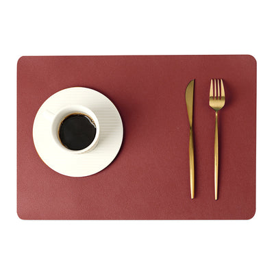 Sottopiatto in ecopelle monocolore bordeaux con tazza di caffè su piattino bianco e posate dorate.